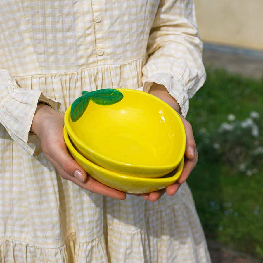 Tre gule keramikk skåler fra Capri Collection, holdt av en person iført en rutete kjole, i en hage.
