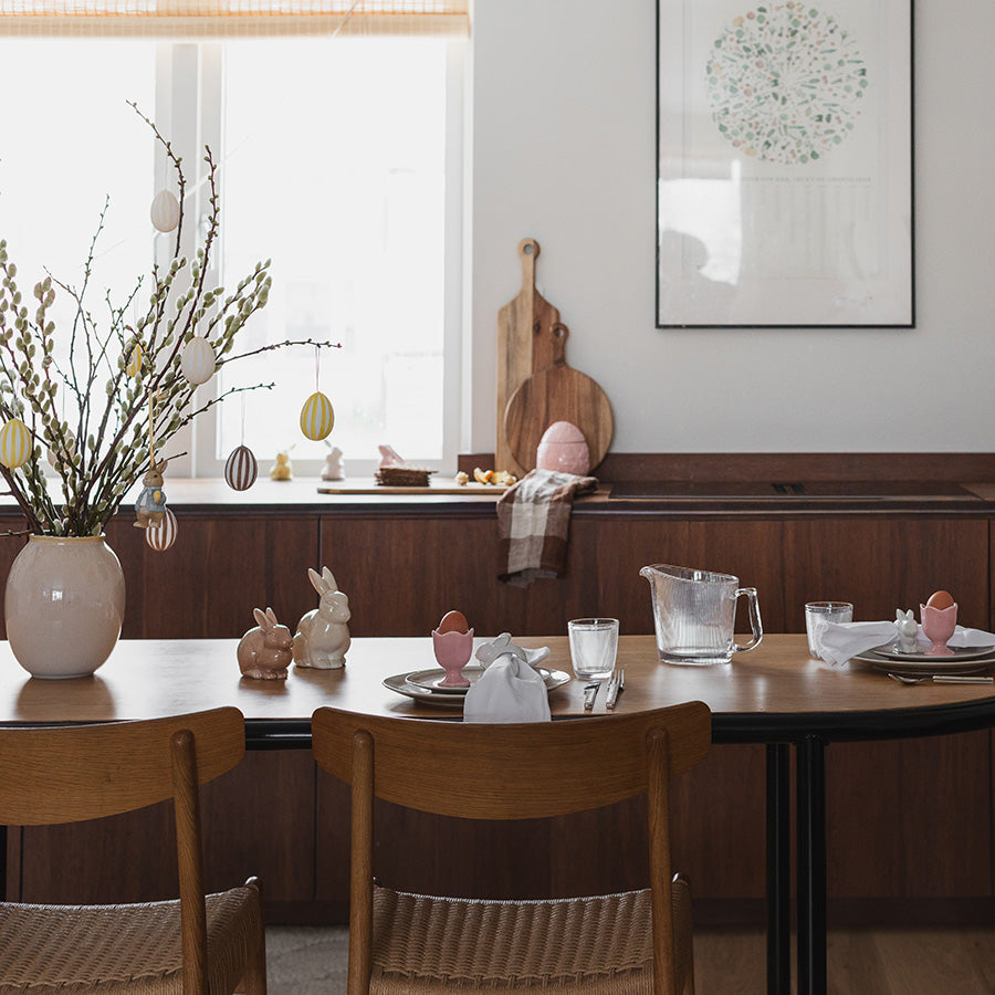 Elegant påskebord med dekorasjoner inkludert fargerike egg og harefigurer, skaper en vårstemning.