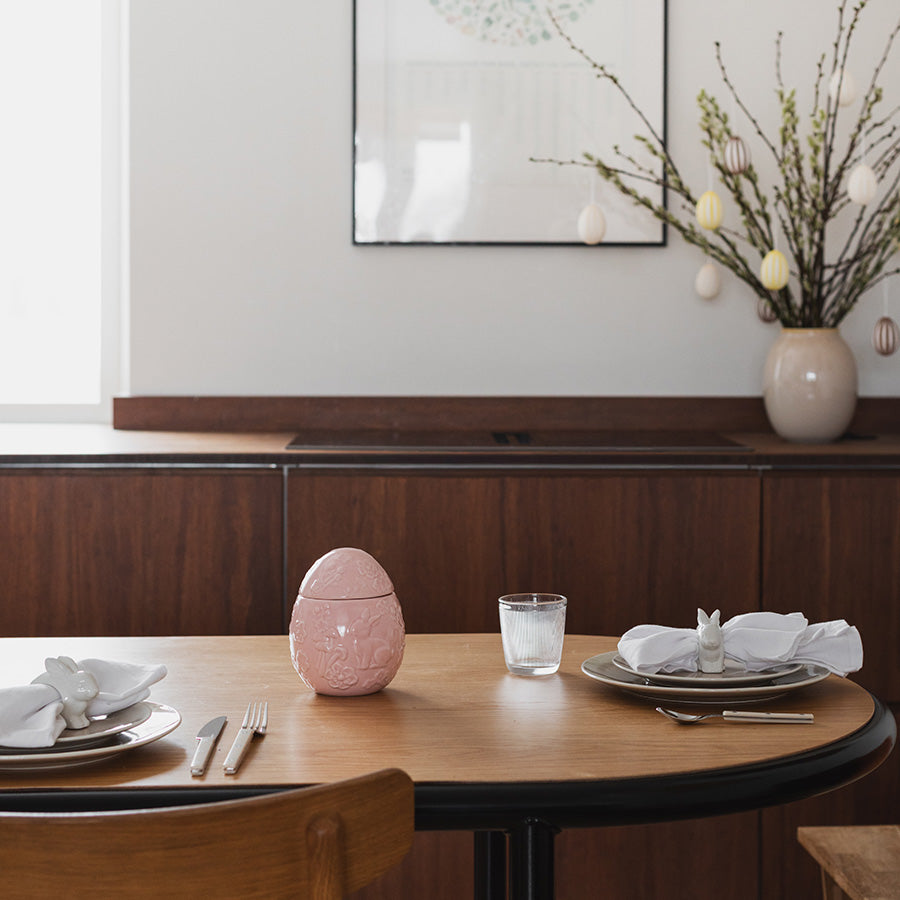 Elegant rosa påskeegg på et middagsbord, dekorert med blomster- og hare-design, perfekt som påskepynt.