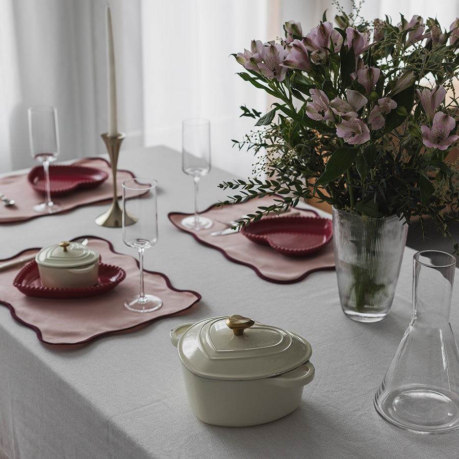 Elegante hjerteformede støpejernsgryter på et dekket bord med blomster og glass, ideelle for festlig servering.