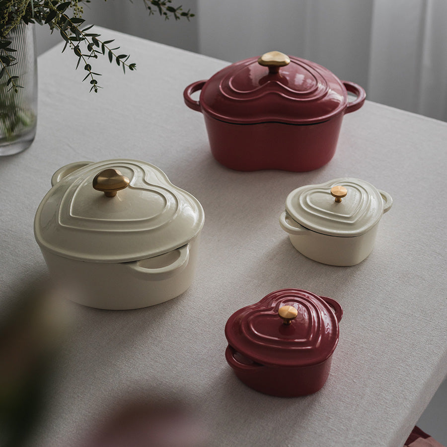 Et sett med hjerteformede støpejernsgryter i krem og rød, perfekt for gryteretter og dekorative gaver.