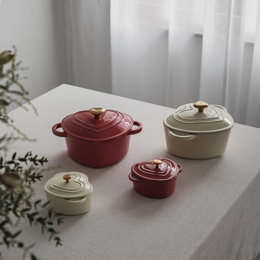Ulike størrelser av hjerteformede støpejernsgryter, inkludert en bringebærrød gryte, perfekt for ulike matlagingsbehov.