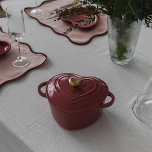 Støpejernsgryte i hjerteform på et dekorert bord med blomster og glass, ideell for romantiske middager.