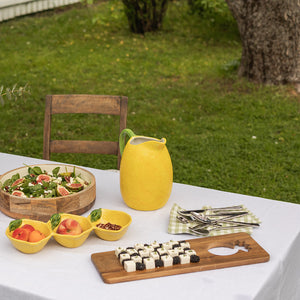 Fjøl i akasie på et bord i hagen, omringet av frisk salat, fruktboller og en gulterrakottakanne, skaper en innbydende sommerstund.