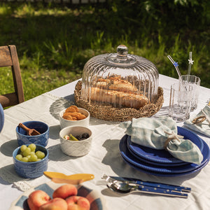 Fat med glasslokk fra Seasons Summer Collection som viser kaker og snacks, sammen med fargerike tallerkener og glass på et dekorerte bord utendørs.
