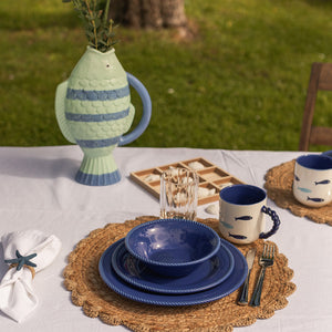 Et dekket bord med marineblå tallerken fra Seasons Summer Collection, omringet av en dekorativ fiskekanne og glass, ideelt for sommerlige måltider.