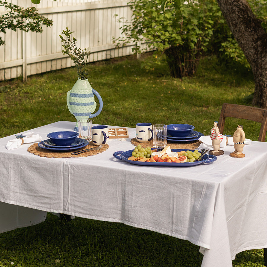 Et elegantr dekket bord med marineblå tallerken fra Seasons Summer Collection, servert med frukt og snacks, under et tre i hagen.