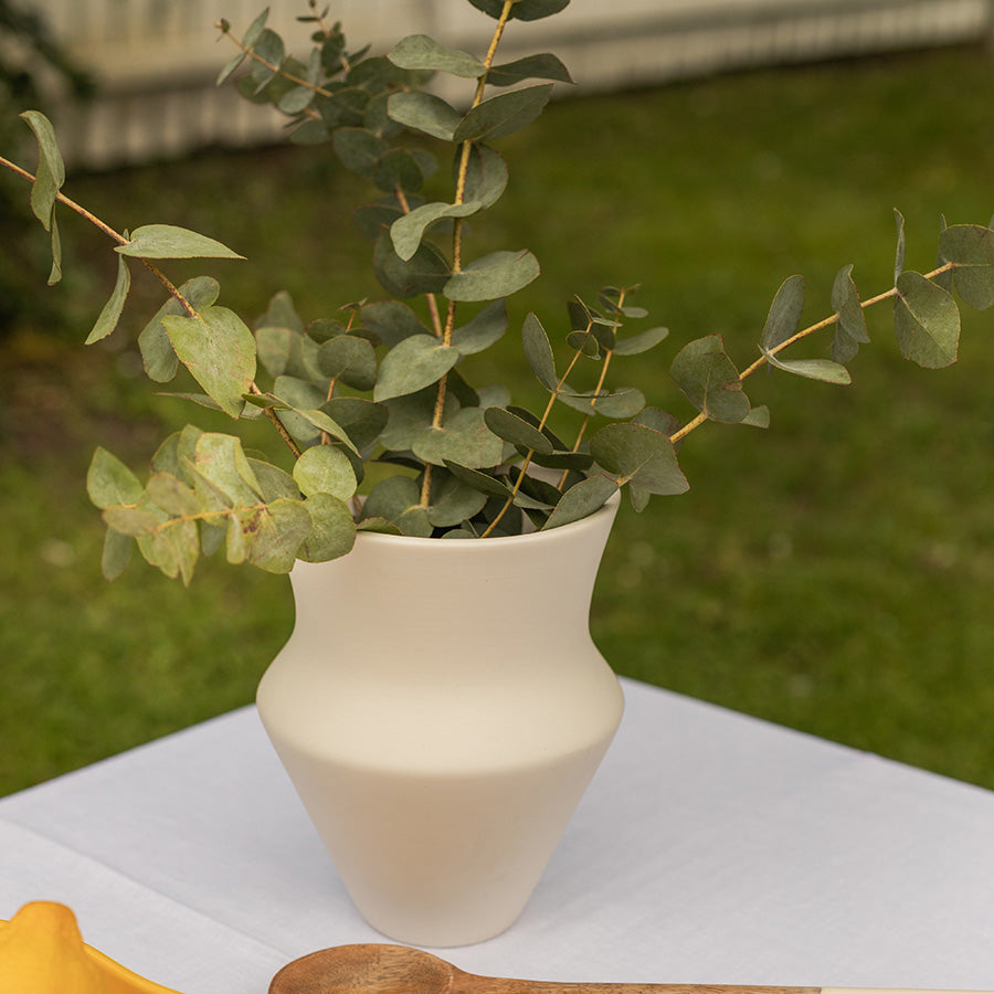 Vase i keramikk med matte overflate, fylt med eucalyptus, plassert på et hvitt bord i en hage.