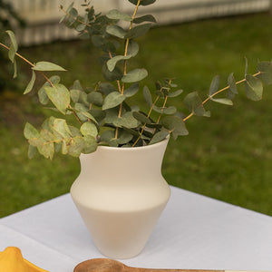 Vase i keramikk med matte overflate, fylt med eucalyptus, plassert på et hvitt bord i en hage.