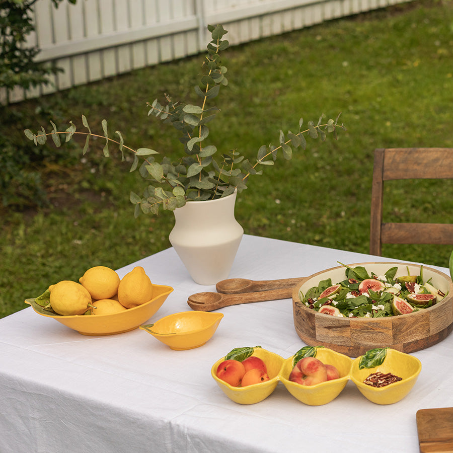 Vase i keramikk på et bord sammen med fruktskåler av gult design, holder eucalyptus og gir en sommerlig stemning.