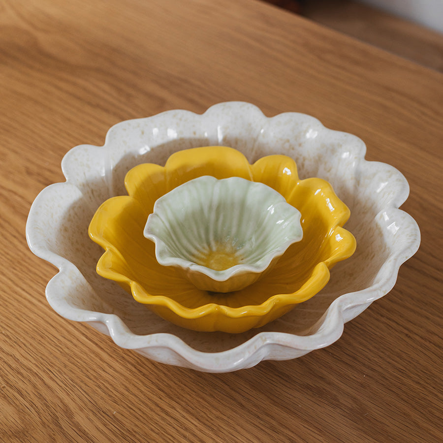 Nærbilde av tre blomsterformede skåler i steingods i gult, hvitt og grønt, fra Seasons Spring Collection, perfekte for elegant borddekking.