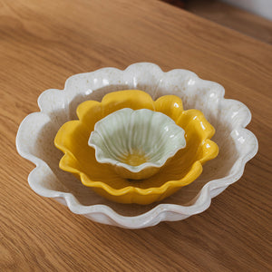 Nærbilde av tre blomsterformede skåler i steingods i gult, hvitt og grønt, fra Seasons Spring Collection, perfekte for elegant borddekking.