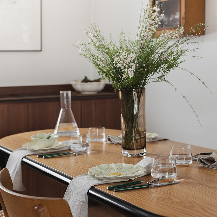 Seasons Spring Collection blomsterformet tallerken 21cm Grønn sett på et lys bord med en vase med blomster, er perfekt for hyggelige måltider.