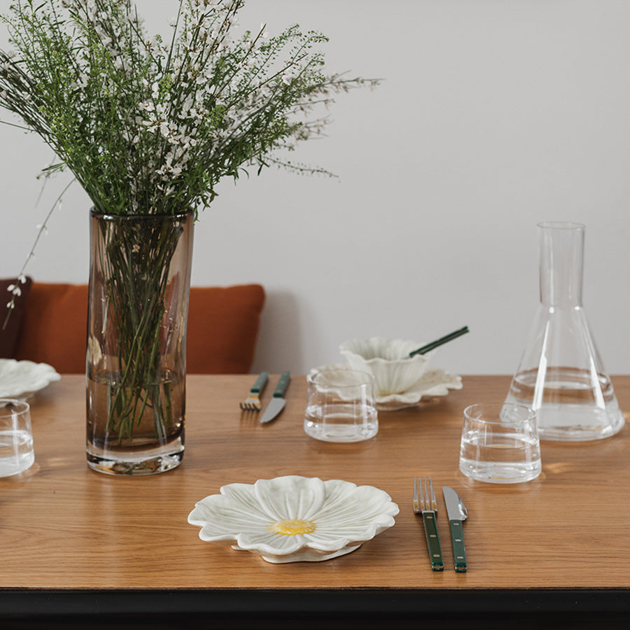 Elegant borddekorasjon med blomsterformet tallerken, blomster og glass på et trebord.