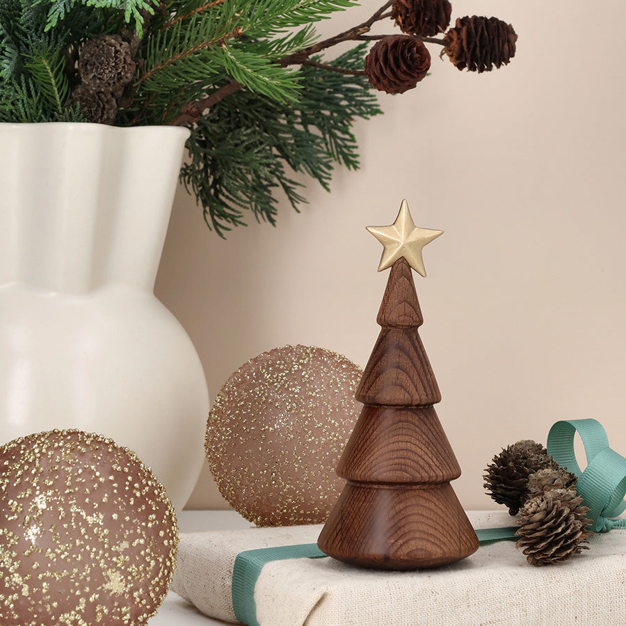 Minimalistisk juletre i termobøk med gullstjerne, plassert på bord med juledekorasjoner og grønt.