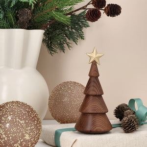 Minimalistisk juletre i termobøk med gullstjerne, plassert på bord med juledekorasjoner og grønt.