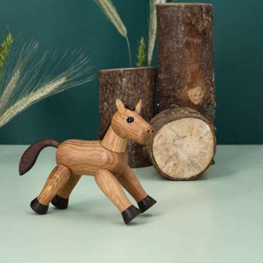SPRING COPENHAGEN Spring Copenhagen Wooden Figures Comet – trehestfigur i naturlige farger som Comet, plassert ved trestammer og dekor i blågrønt rom