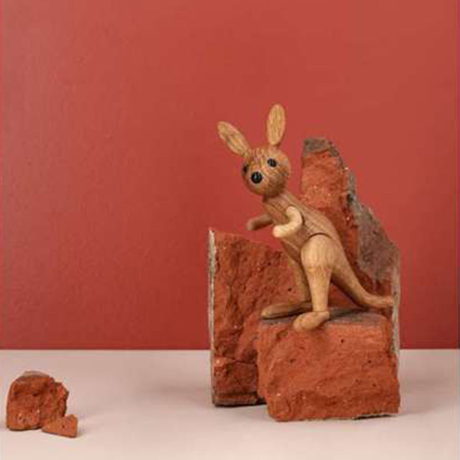 SPRING COPENHAGEN: Spring Copenhagen Wooden Figures Roo – tre-kenguru Roo sittende på kubbe, dekorativ interiørdetalj mot rød bakgrunn