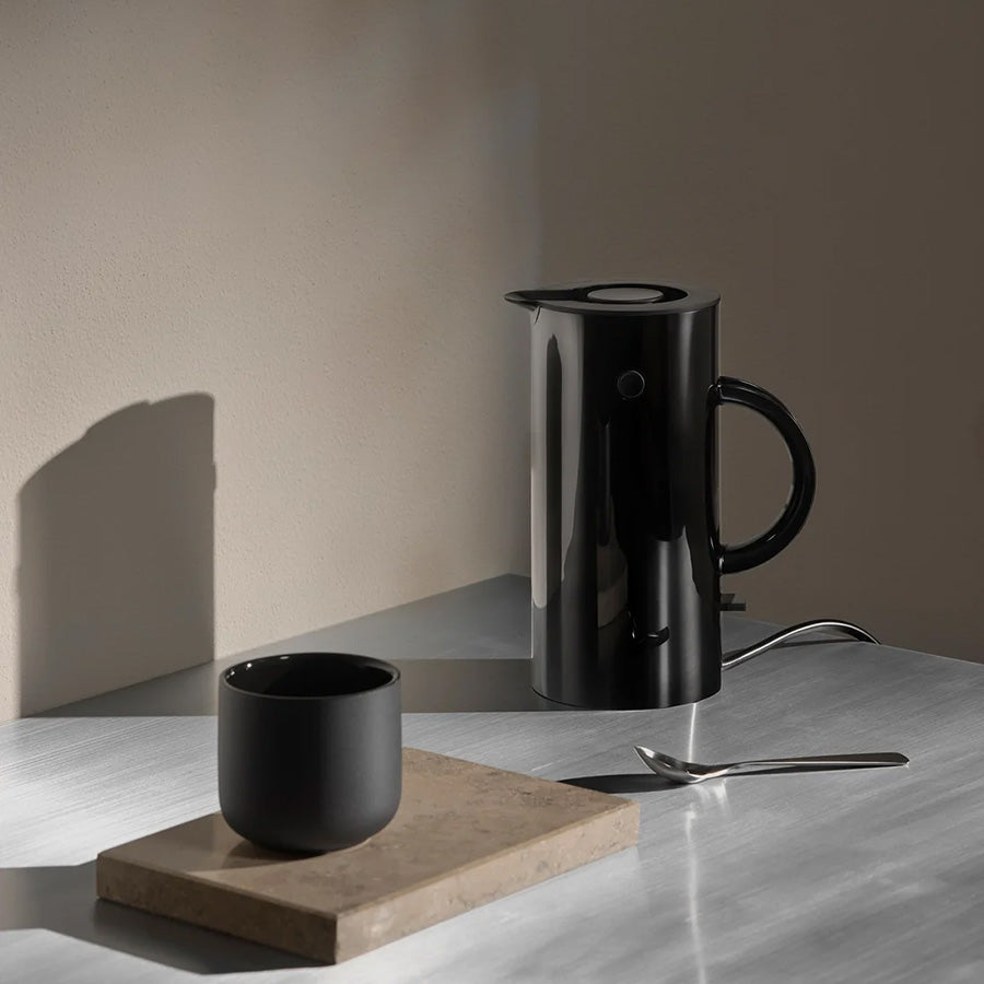 Svart Stelton EM77 Mini vannkoker på bord med kopp og skje i varmt lys