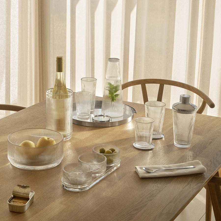 Et sett med stilige drikkeglass sammen med en vase og en shaker på et trebord, perfekte drikkeglass for festmiddagen.