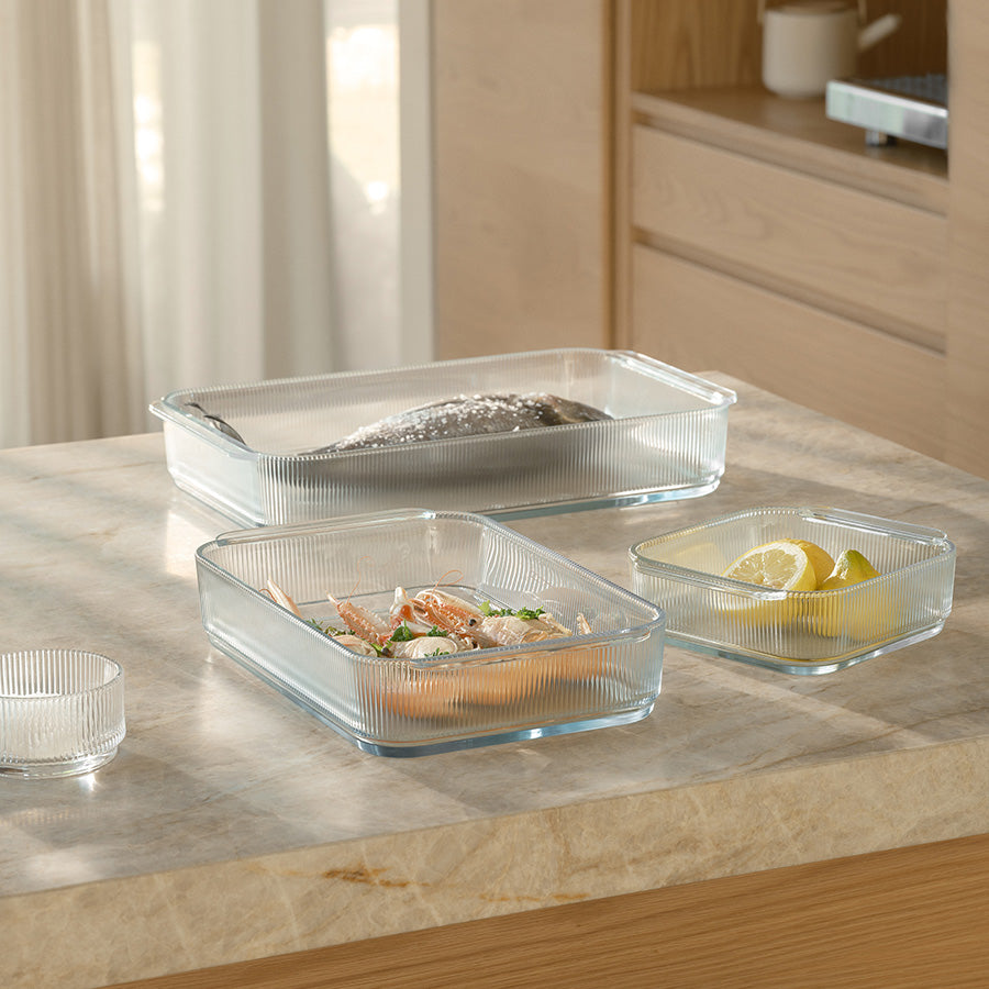 Ulike størrelser av Stelton Pilastro ildfaste former i klar glass, med fersk fisk og sitron, ideell for matlaging.