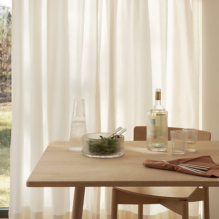 Elegant bordoppsett med Stelton Pilastro serveringsbolle, dekorert med grønn salat og glassvann på et lyst trebord.