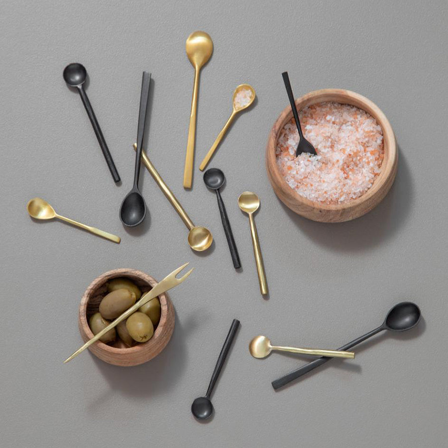 Variasjon av serveringsskjeer i gull, metall og sort, sammen med små boller med oliven og salt, for en stilfull borddekking.