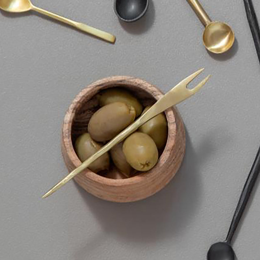 Gylden serveringsgaffel plassert i en trekopp fylte med oliven, som viser den allsidige bruken av serveringsgaffel.