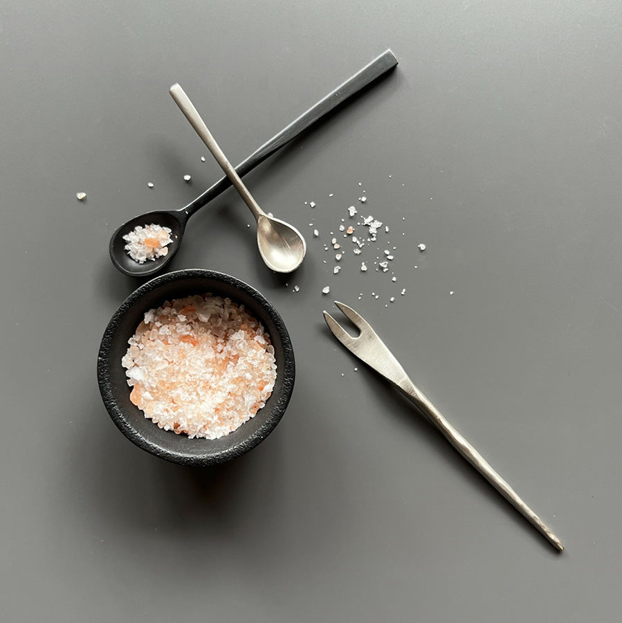 Serveringsgaffel i rustikk metall sammen med salt og tilbehør på mørk overflate, perfekt for stilfull servering.