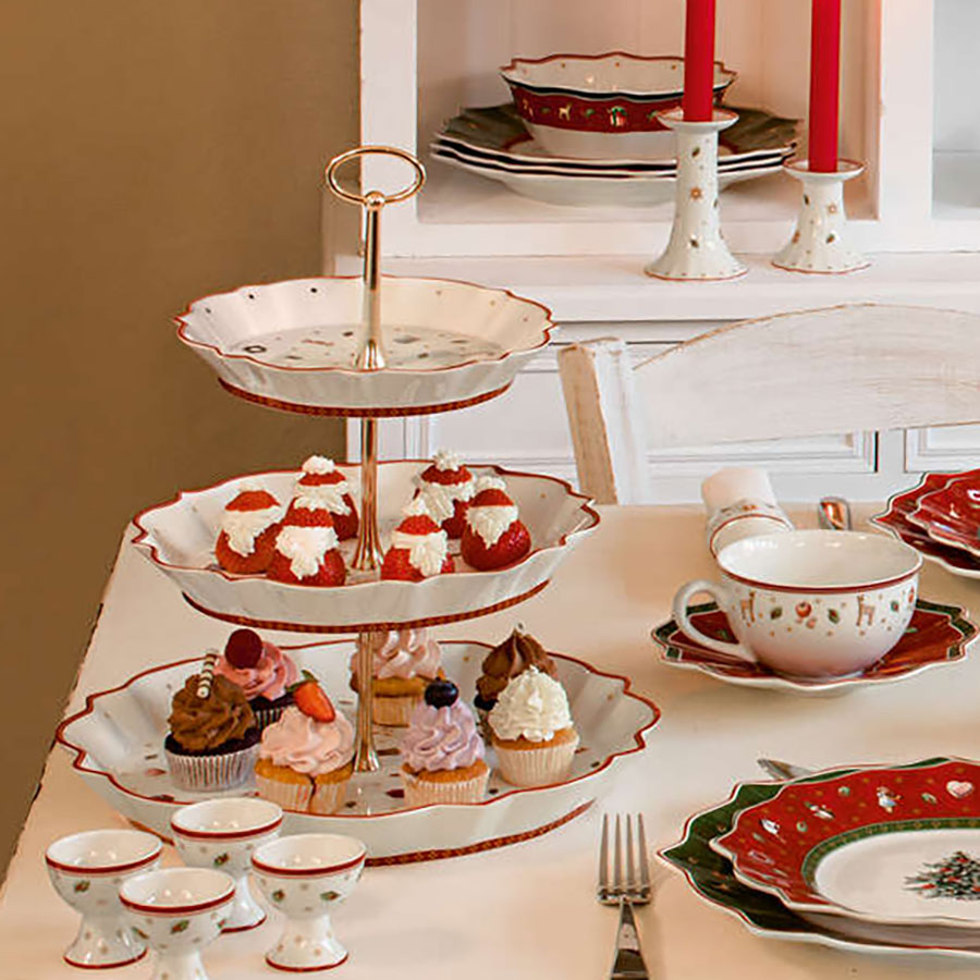 Villeroy & Boch Toys Delight etasjefat på festbord, fylt med cupcakes og delikate julekaker, sammen med julepyntede tallerkener.