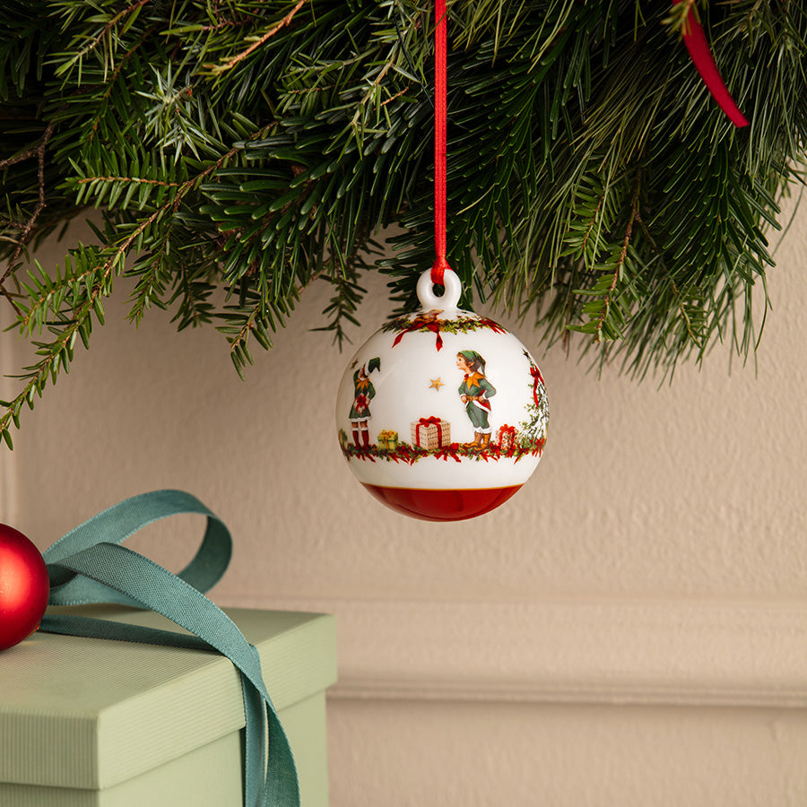 Årets julekule 2026 fra Villeroy & Boch henger på juletregrener med nisser, julegaver og røde detaljer