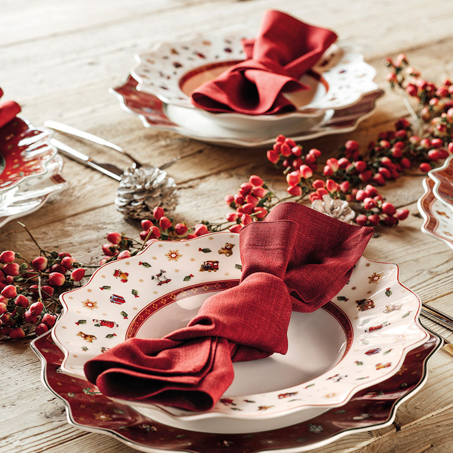 Villeroy & Boch Toy's Delight dyp tallerken satt på bord med røde servietter, omkranset av juleroser og julepynt for en feiring.