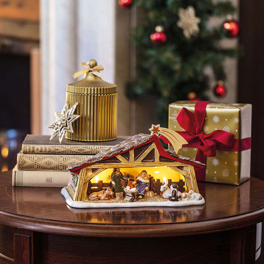 Stemningsfull Villeroy & Boch julekrybbe med innvendig belysning, perfekt som juledekorasjon og gavesett, plassert på et bord med julegave og dekor.