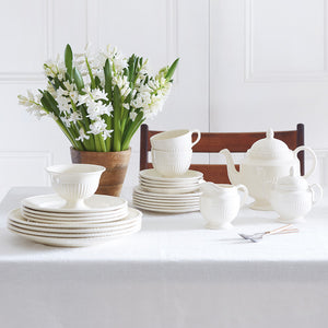 Samling av Wedgwood Edme Plain Tekanne, kopper og tallerkener på et bord med blomster som dekorasjon.