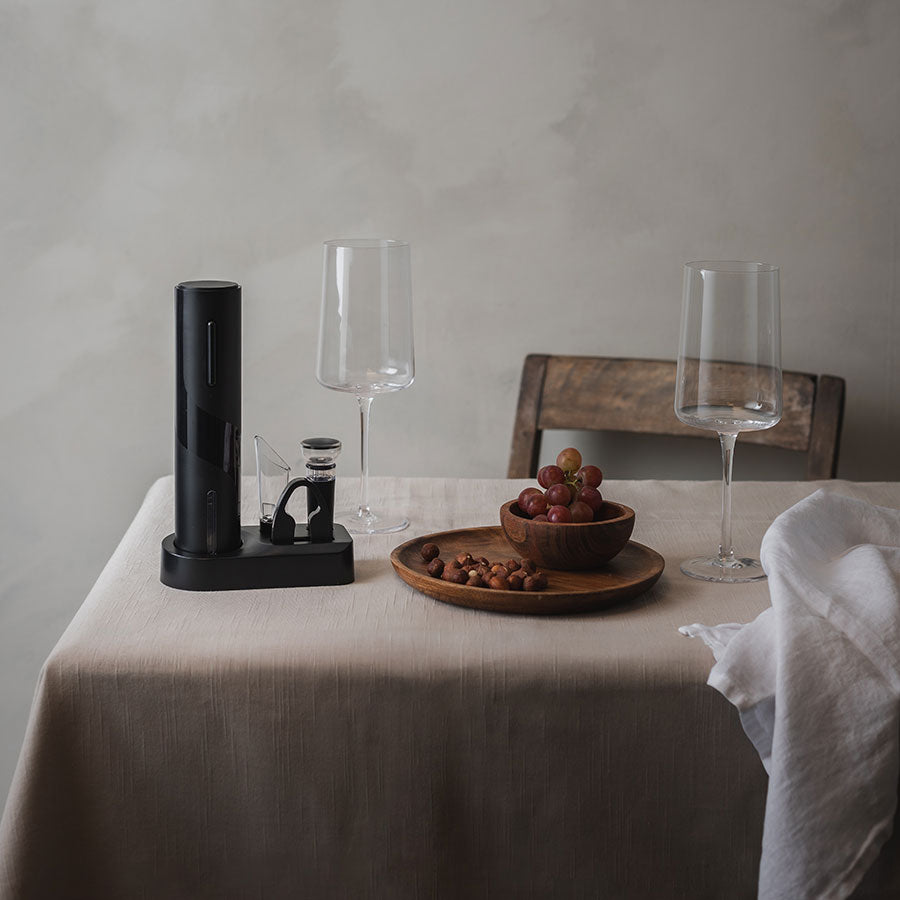 Winery elektrisk vinåpner satt opp på bord med to vinglass, en skål med druer og nøtter, noe som skaper en elegant vinopplevelse.