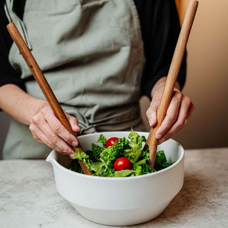 Hender bruker salatbestikk i akasietre til å vende en frisk salat i bolle